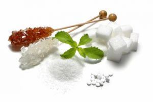 Zuckeralternative: Brauner Kandis, Zuckerkristalle, Süßstoff Acesulfam, Sucolin und Birkenzucker auf einem Tisch.
