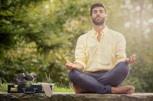 Mann im Anzug meditiert neben Aktentasche.