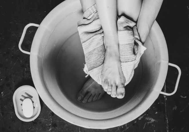 Schwarzweißfotografie von Füßen, die in einem Bottich gewaschen werden