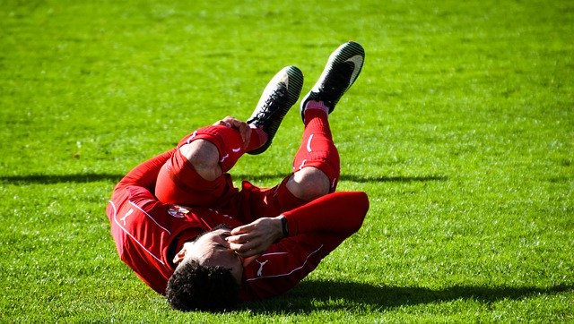 Fußballspieler liegt auf dem Feld und hält sein verkrampftes Bein
