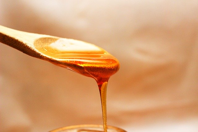 Honig rinnt von einem Holzlöffel in ein Gefäß