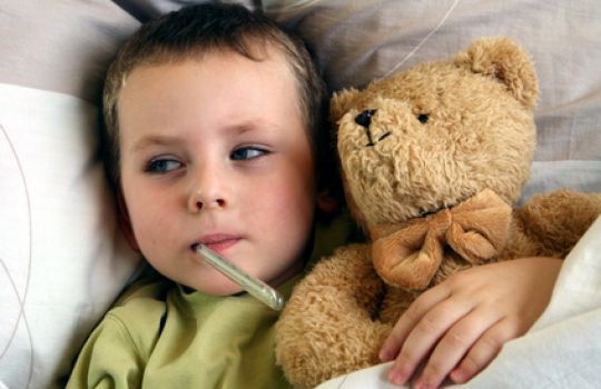 Krankes Kind mit Fieberthermometer und Teddy im Bett. 