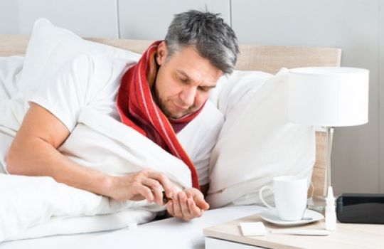 Mann liegt erkältet im Bett.
