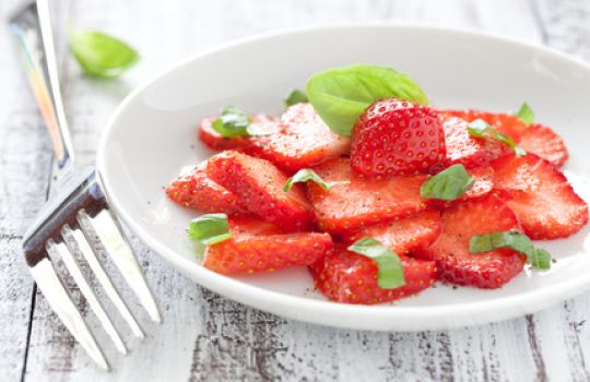 Ein Teller Erdbeeren mit Basilikum garniert.