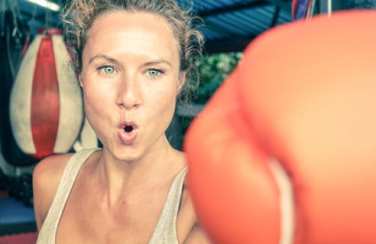 Ein Frau mit Boxhandschuhen führt einen Schlag durch.