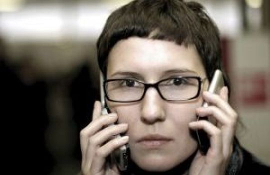 Frau mit Brille und zwei Handys an den Ohren