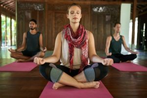 Drei Personen auf Yogamatten in meditativer Position.