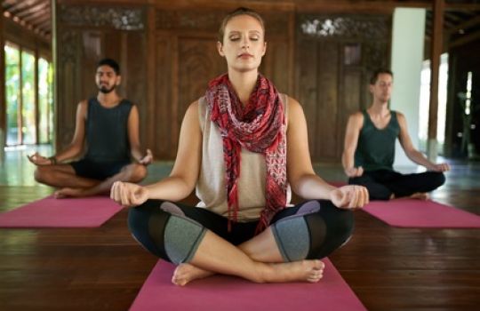 Drei Personen auf Yogamatten in meditativer Position.