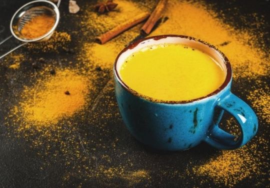 Blaue Tasse gefüllt mit goldener Milch, umgeben von Zimt/Kurkuma-Pulver