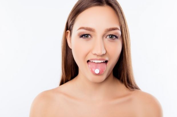 Eine Frau hat eine Tablette Schüßler Salze auf ihrer ausgestreckten Zunge und zeigt sie hervor.