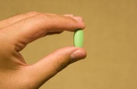 Nahaufnahme einer Hand, die eine grüne Tablette zwischen Daumen und Zeigefinger hält.