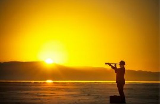 Mann mit Fernrohr steht vor Sonnenuntergang am Strand