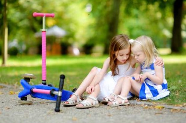 Junges Mädchen tröstet ihre Schwester, diese hat eine kleine Wunde auf dem Knie.