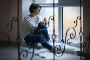 Depressive Frau sitzt mit trüben Gedanken am Fenster.