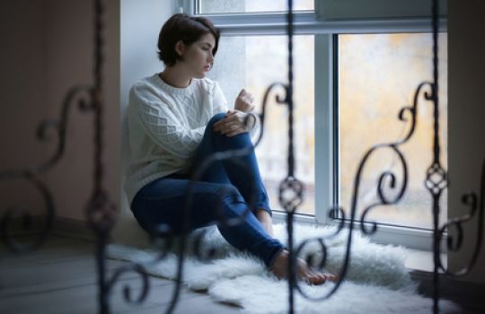 Depressive Frau sitzt mit trüben Gedanken am Fenster.