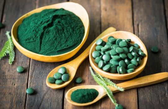 Foto einer Schale von Spirulinatabletten und gemahlenem Spirulina in Holzschalen