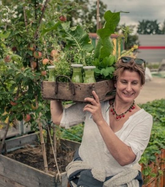 Gabriele Bräutigam mit einer Holzkiste voll mit Smoothies und Wildkräutern.