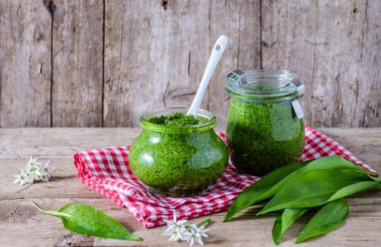 Bärlauchpesto-Weckgläser auf rot-weiß-kariertem Tuch mit Bärlauch-Blättern.