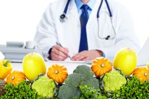 Ein im Arztkittel verkleideter Mann sitzt hinter einem Tisch voller Gemüse.