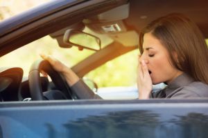Junge Frau fährt Auto und gähnt - ausgeprägte Tagesschläfrigkeit ist gefährlich.