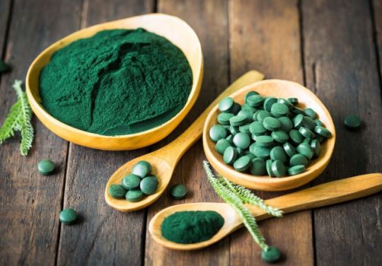 Foto einer Schale von Spirulinatabletten und gemahlenem Spirulina in Holzschalen