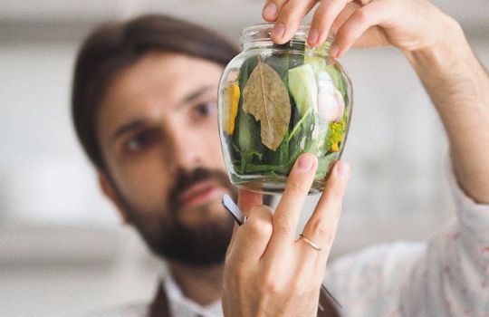 Mann hält Glas mit Kräutern drin hoch