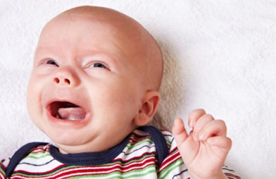 Ein Baby liegt schreiend auf einer Decke.