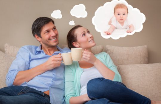 Junges Paar sitzt auf dem Sofa, in einer Gedankenblase ist ein Baby zu sehen.