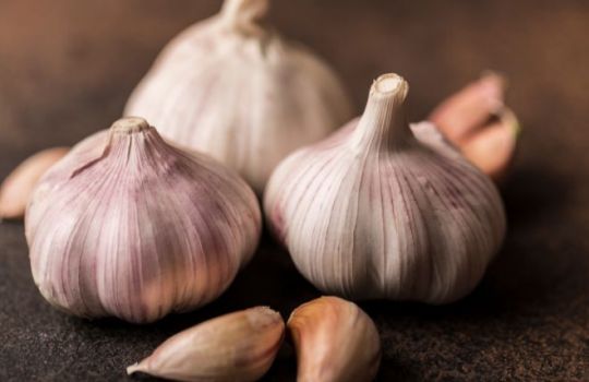 Foto von drei Knollen Knoblauch und einzelnen Zehen auf hölzernem Untergrund