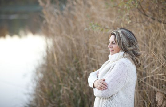 Frau im Wollpullover schaut auf den See und schlägt der Herbstdepression ein Schnippchen.