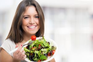 Eine Frau isst einen grünen Blattsalat mit kleinen Tomaten.