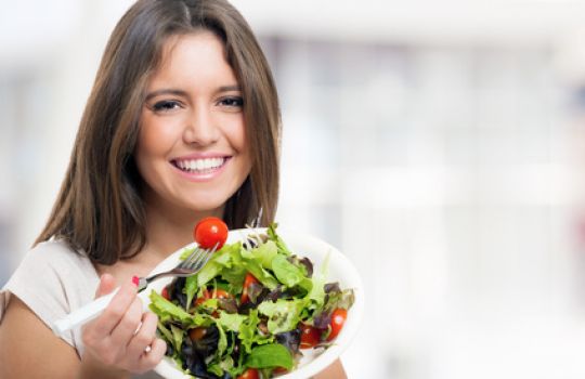 Eine Frau isst einen grünen Blattsalat mit kleinen Tomaten.