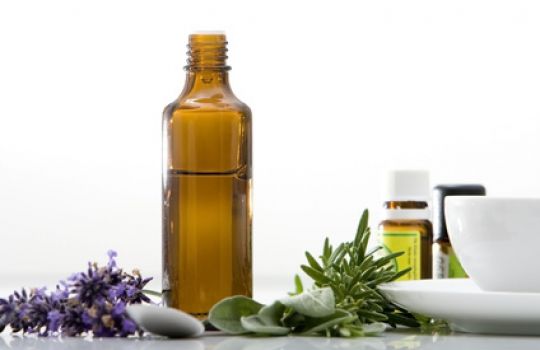 Eine Flasche mit ätherischen Ölen steht zwischen Lavendel und anderen Duftpflanzen auf dem Tisch.