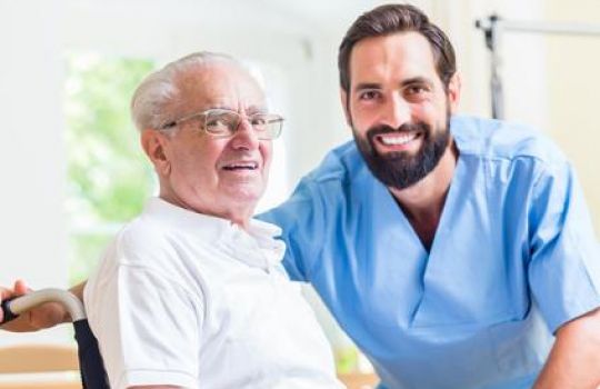 Pfleger und Parkinsonerkrankter lächeln in die Kamera