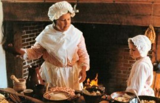 Eine alte Küche sowie eine Frau und ein kleines Mädchen in älterer Kleidung sind zu sehen.