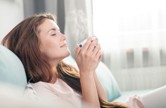 Junge Frau sitzt auf dem Sofa und genießt die wohltuende Wärme und den Duft einer Tasse Tee.