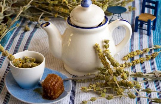 Griechischer Bergtee in einer Teetasse mit Honig. Im Hintergrund eine Teekanne.